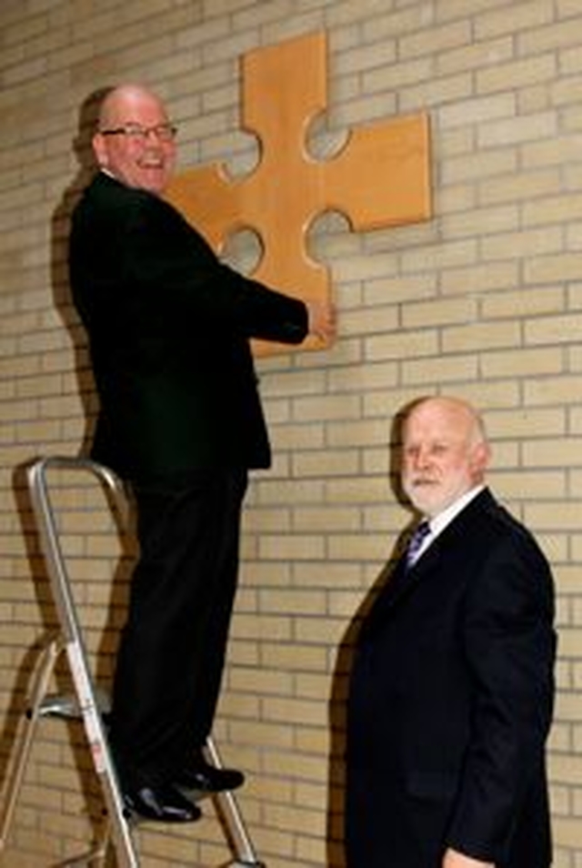 Fred Deane and Jim Kieran putting the cross carved by young people involved with Solas Project up in St Ann’s parish hall. 